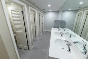 Restroom sink counter facing white louvered stalls