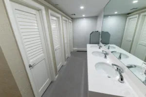 Restroom sink counter facing white louvered stalls
