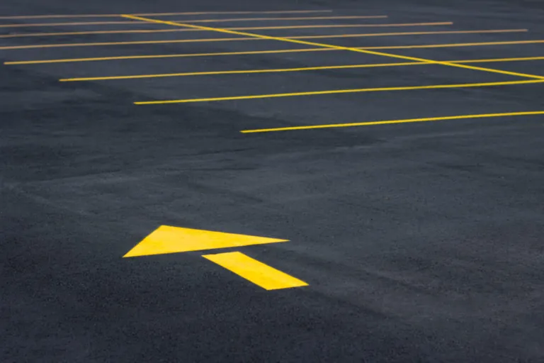 Yellow directional arrow and stall lines on parking lot pavement